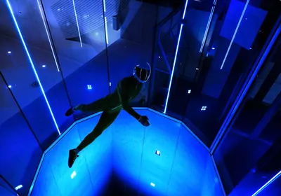 A person skydives indoors among blue lighting.